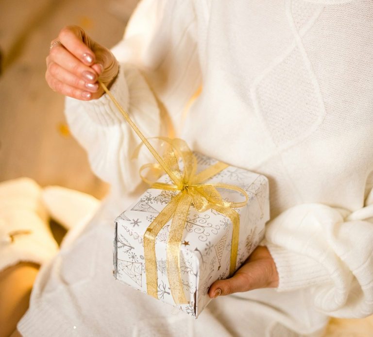 Woman opening a present Woman in luxurious wool jumper sat on the floor opening a present wrapped in white paper and a gold ribbon.