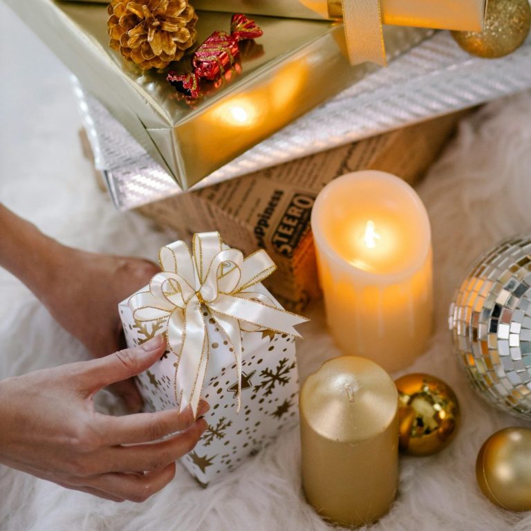 Person with a Christmas present, wrapped in white paper and a gold bow. Person with a Christmas present, wrapped in white paper and a gold bow, with candles and baubles next to the present.