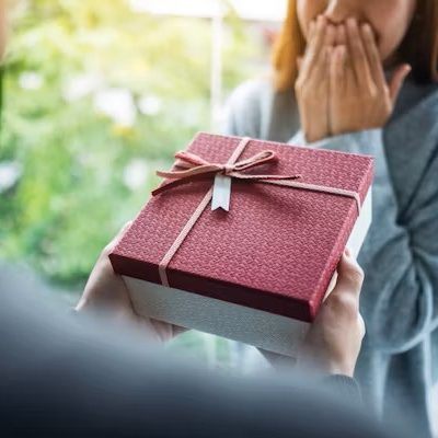 Woman receiving a surprise gift wrapped in a pink and red box and a material bow with matching gift tag.